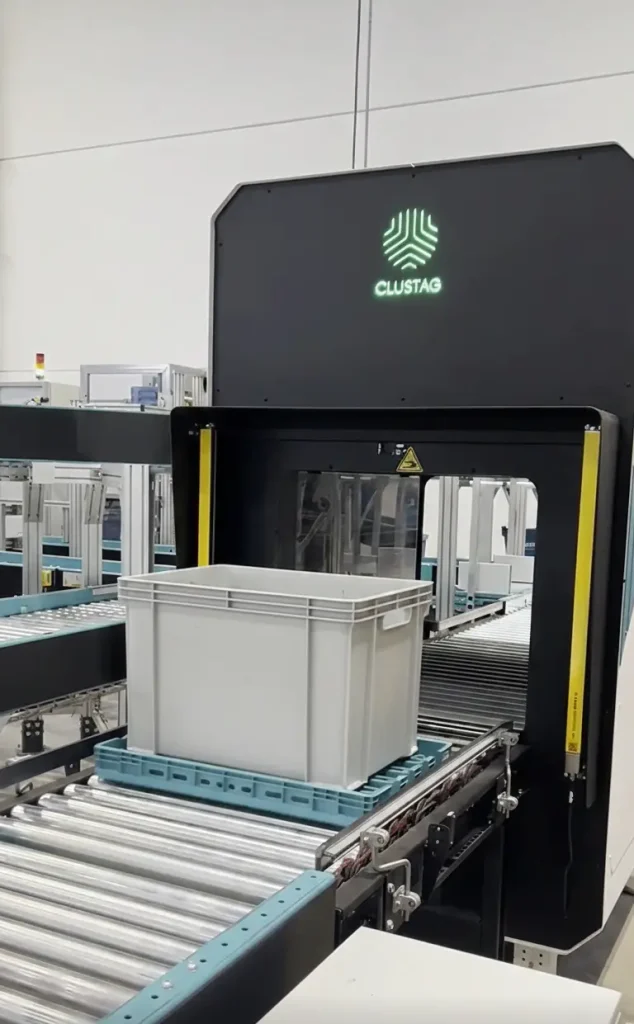 Automated RFID infeed station by Clustag scanning a plastic tote on a conveyor inside a warehouse.