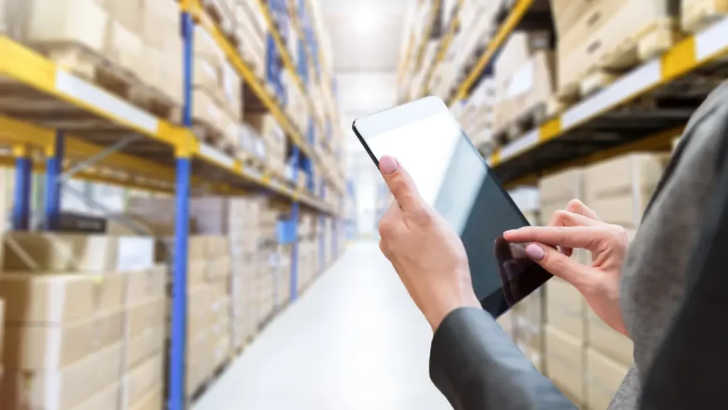 Soluciones RFID en retail para la gestión de inventario en tiempo real en almacenes Mano usando una tablet en un pasillo de almacén, demostrando soluciones RFID en retail para el seguimiento de inventario en tiempo real.