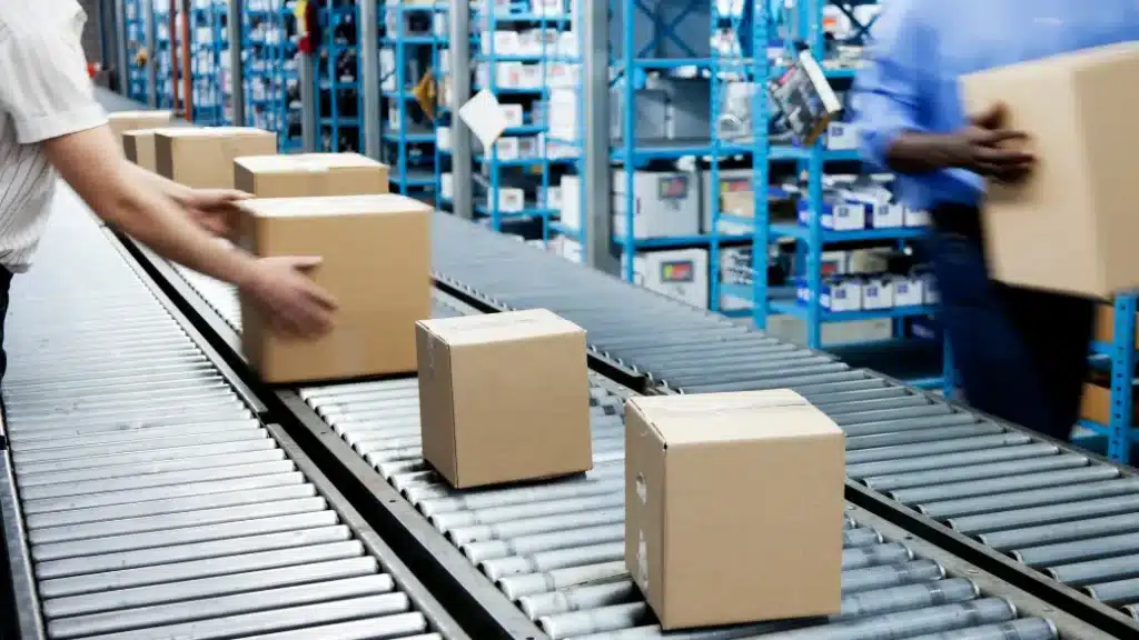 Soluciones RFID en retail para optimizar el procesamiento de pedidos mediante cintas transportadoras Cajas de cartón moviéndose en una cinta transportadora en un centro de distribución, mostrando soluciones RFID en retail para la verificación automatizada de envíos.