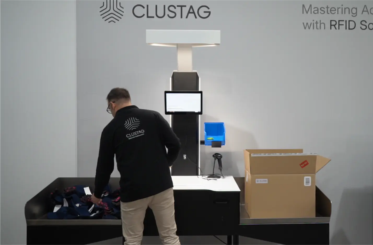 Persona utilizando un sistema RFID de Clustag para la gestión de pedidos, con una caja de cartón sobre la mesa y una pantalla táctil en primer plano.